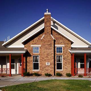 A brick house with a gable roof and a porch in front, set against a clear blue sky.