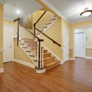 A well-lit residential hallway featuring a wooden staircase with white railings.