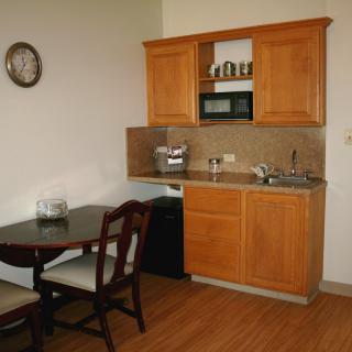 A small kitchenette with wooden cabinets, a microwave, and an adjacent dining area.