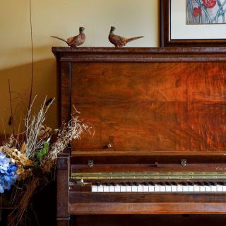 A vintage wooden piano adorned with decorative birds and a floral arrangement, accompanied by framed artwork on the wall.