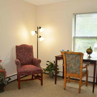 A cozy home office with a desk, two chairs, a lamp, and indoor plants by the window.