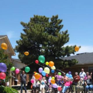 A group of people gather outdoors, releasing colorful balloons into the sky.