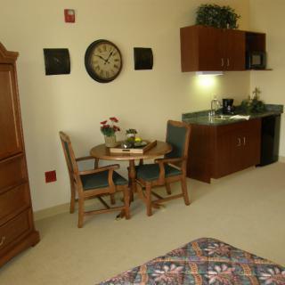 A cozy hotel room interior with a table, chairs, wall clock, and cabinetry.