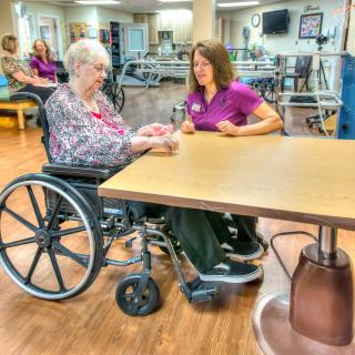 A caregiver assists an elderly person in a wheelchair at a nursing home.