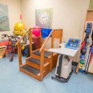 A physical therapy room equipped with exercise equipment, including a set of stairs, various balls, and mobility aids.