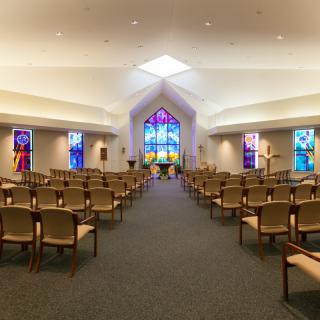 Interior view of a chapel with rows of chairs and colorful stained glass windows.