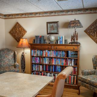 A cozy living room featuring a bookshelf filled with books, comfortable chairs, and warm lighting.