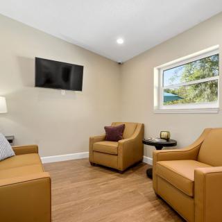 A cozy living room with two armchairs, a television mounted on the wall, and a window allowing natural light to fill the space.