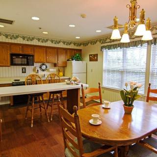 A cozy kitchen and dining area with wooden furniture, featuring a chandelier, decorative plants, and various kitchen appliances.