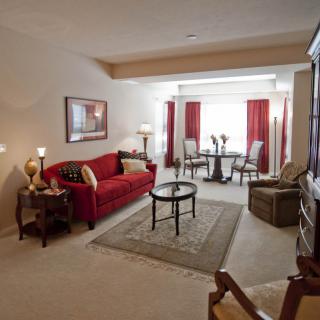 A cozy living room with a red sofa and a dining area in the background.