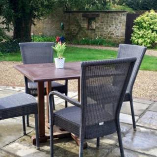 A cozy outdoor patio setup with a table and four chairs, surrounded by a garden.