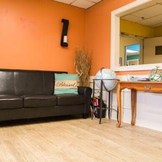A cozy waiting area featuring a black leather couch, decorative elements, and an inviting orange wall.