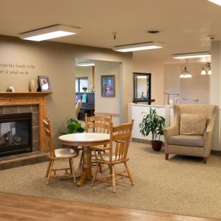 A cozy living room with a fireplace, table, chairs, armchair, and plants.