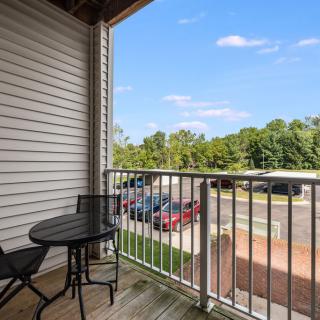 A view from a balcony with seating overlooking a parking lot and trees under a clear blue sky.