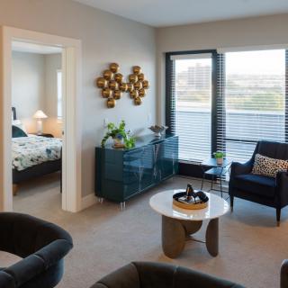 A modern living room with stylish furniture, indoor plants, and a view into the bedroom.
