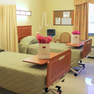 A clean and well-organized hospital patient room with two beds and flowers on the tables.