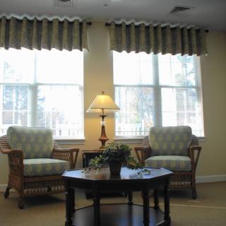A cozy living room with two chairs, a table, and a lamp in front of large windows.