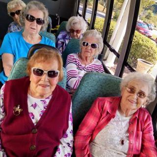 A group of elderly women wearing sunglasses seated on a bus.