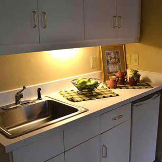 A kitchen counter with a sink, cabinetry, and a fruit bowl under soft lighting.