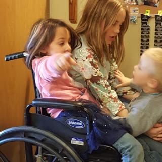 Three children share a moment of play and interaction in a wheelchair.