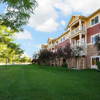 A view of an apartment building with a manicured lawn and trees on a sunny day.