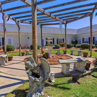 A serene courtyard with a pergola, stone benches, and decorative sculptures.