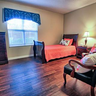 A cozy bedroom with a single bed, armchair, and wooden flooring.