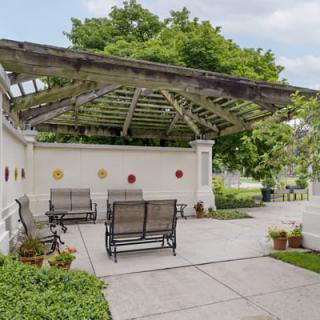 A tranquil garden patio with a pergola and benches surrounded by greenery.
