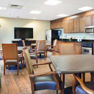 A modern dining and kitchen space featuring a television, multiple tables and chairs, wooden flooring, and built-in cabinets.