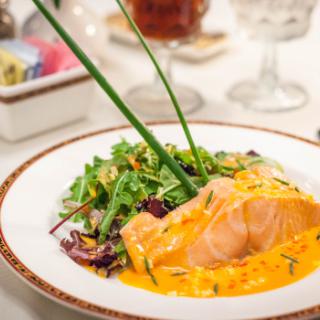 A gourmet plate featuring salmon with a rich orange sauce, accompanied by a fresh salad garnish.