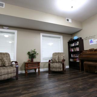 A cozy living room with chairs, a bookshelf, and a piano.