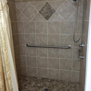 A tiled shower with a handrail and showerhead.
