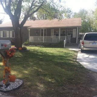 A suburban house with a front yard, driveway, and parked car under a sunny sky.