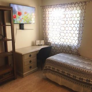 Cozy bedroom with a single bed, desk, bookshelf, and wall-mounted TV.
