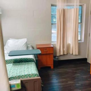 A simple hospital room with a bed, bedside table, and window with curtains.
