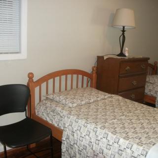 A simple bedroom with two single beds, a chair, and a dresser.