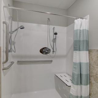 Accessible bathroom with a shower area featuring grab bars, a handheld showerhead, and a bench seat.