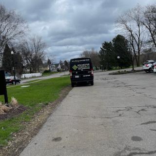 A view of a cloudy day with a parked vehicle on a street surrounded by trees.