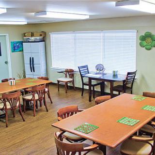 A cozy dining room with wooden tables and chairs, featuring large windows and bright lighting.
