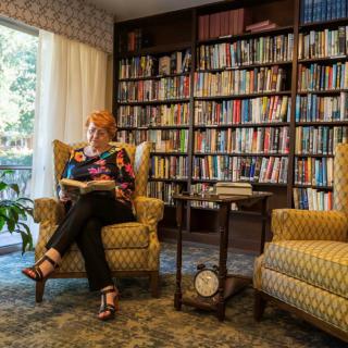 A woman sitting in an armchair reading a book in a cozy library room.