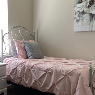 A cozy bedroom with a single bed adorned in pink bedding and decorative pillows, complemented by wall art.
