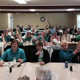 A group of people gathered in a conference room, with many raising their hands.