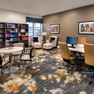 A modern office workspace featuring desks with computers, a bookshelf, and comfortable seating.