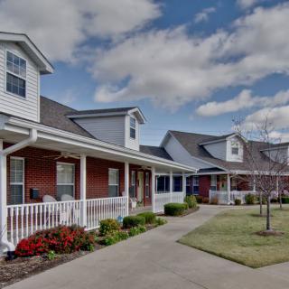 A charming residential building with a porch and a well-maintained lawn under a cloudy sky.