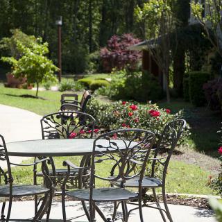 A serene garden setting featuring metal patio furniture surrounded by lush greenery and vibrant flowers.
