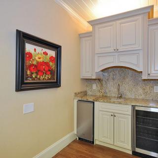 A compact kitchen area with white cabinets, a small refrigerator, and colorful artwork on the wall.