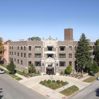 A street view of a residential apartment building with trees and landscaping in front.