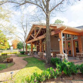 A wooden building with large windows surrounded by trees and a landscaped garden on a sunny day.