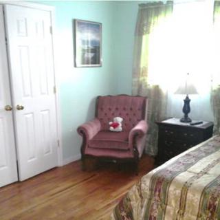 A cozy bedroom featuring an armchair next to a bed, with a lamp on the nightstand by the window.