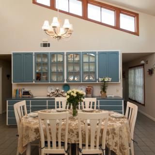 A cozy kitchen with a round dining table, adorned with flowers and surrounded by blue cabinetry.
